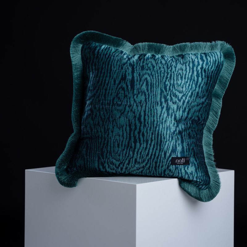 Nati Luxury Pillow Kissen 'Kyoto Turquoise' – petrolfarbener Samt mit Holzmaserungs-Muster und gefranstem Rand, freigestellt auf einem Podest