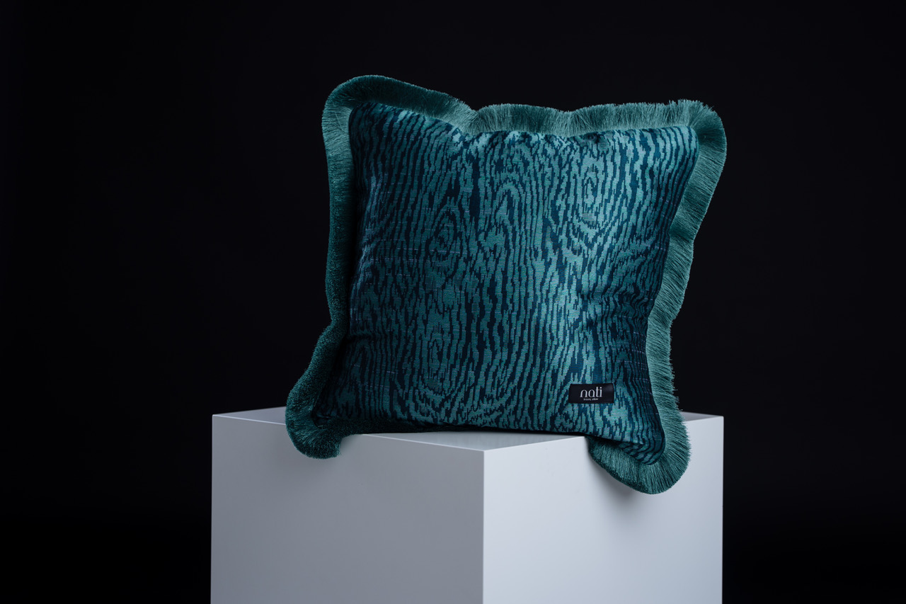 Nati Luxury Pillow Kissen 'Kyoto Turquoise' – petrolfarbener Samt mit Holzmaserungs-Muster und gefranstem Rand, freigestellt auf einem Podest
