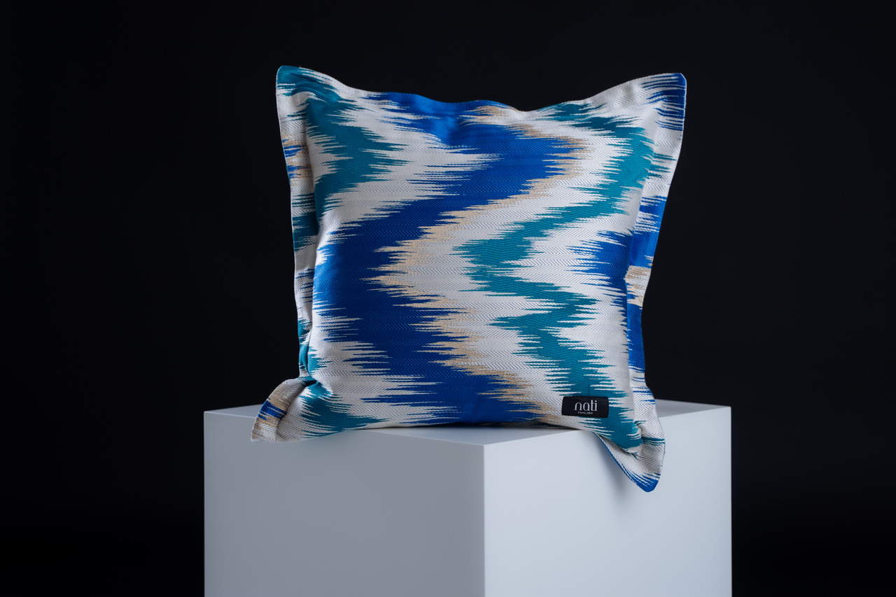 Nati Luxury Pillow Kissen 'Zigzag – Sapphire' – Zickzack-Ikat-Muster in Saphirblau, Türkis und Cremeweiß, freigestellt auf einem Podest