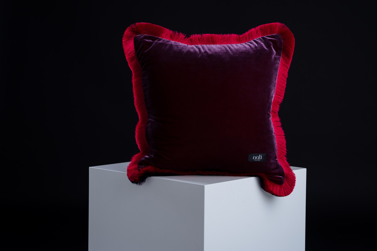 Nati Luxury Pillow Kissen 'Magic – Fleur de grenadier' – auberginefarbener Samt mit rotem Fransenrand, freigestellt auf einem Podest