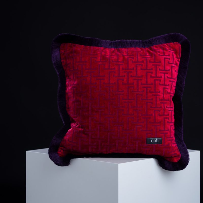 Nati Luxury Pillow Kissen 'Jim Crimson' – karmesinroter Samt mit grafischem Muster und dunklem Samtrand, freigestellt auf einem Podest