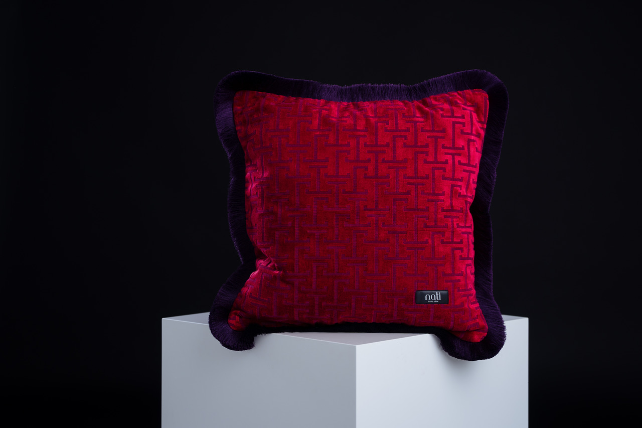 Nati Luxury Pillow Kissen 'Jim Crimson' – karmesinroter Samt mit grafischem Muster und dunklem Samtrand, freigestellt auf einem Podest
